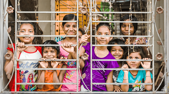 A group of children smiling through a window grate.