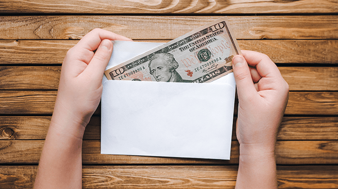 A woman's hand holding a dollar bill in an envelope on a wooden table.